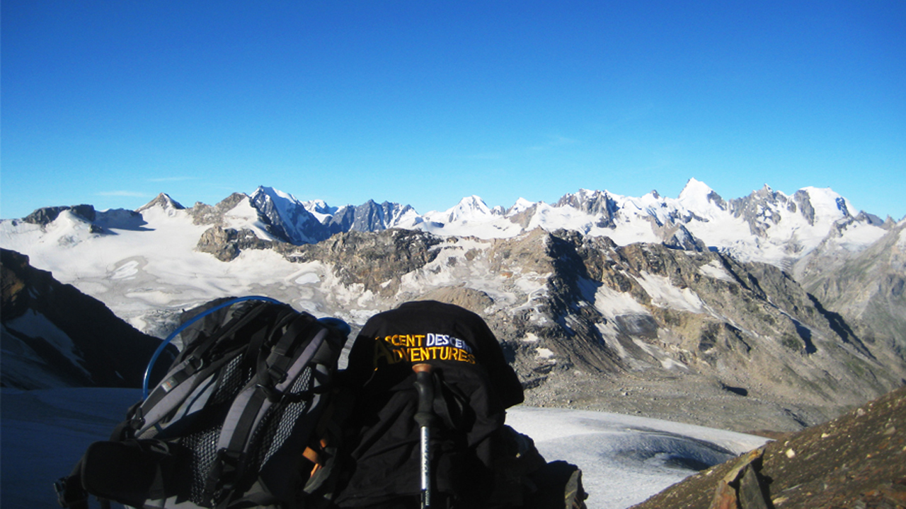 On a mountain summit, a t-shirt with the words Ascent Descent Adventures is laying next to a knapsack.