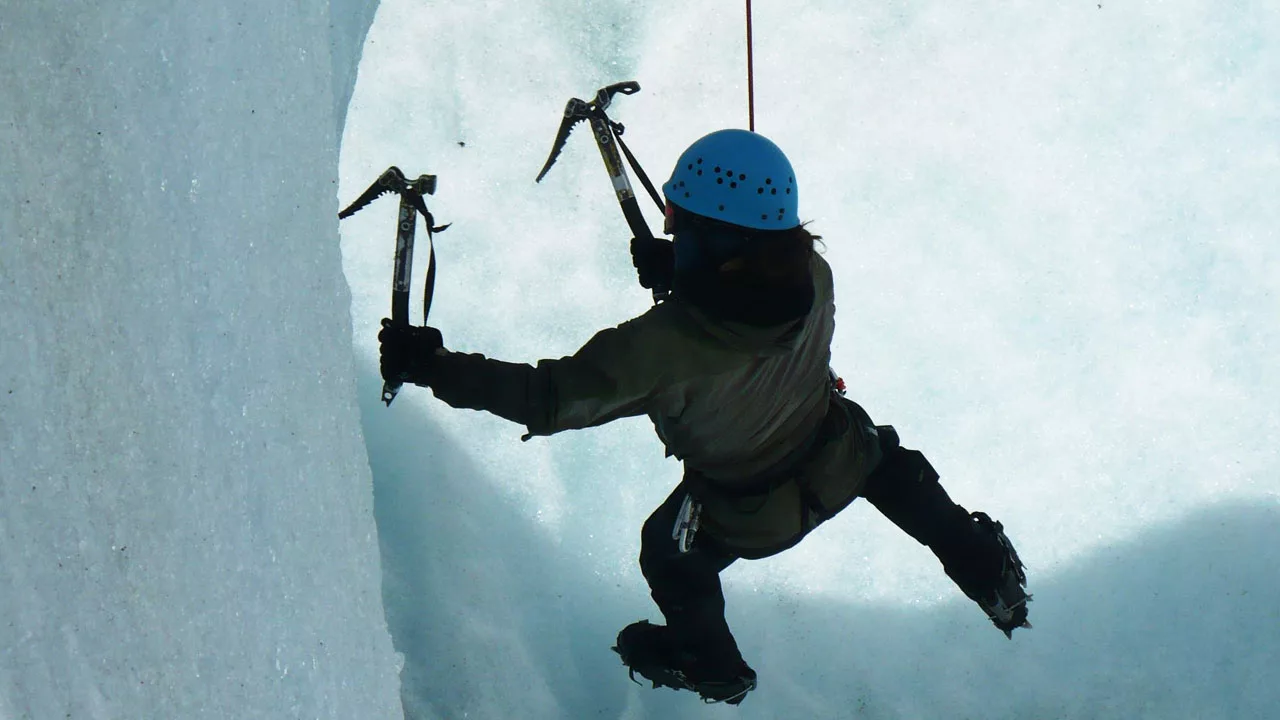 climber hanging on overhang ice wall with ice axe