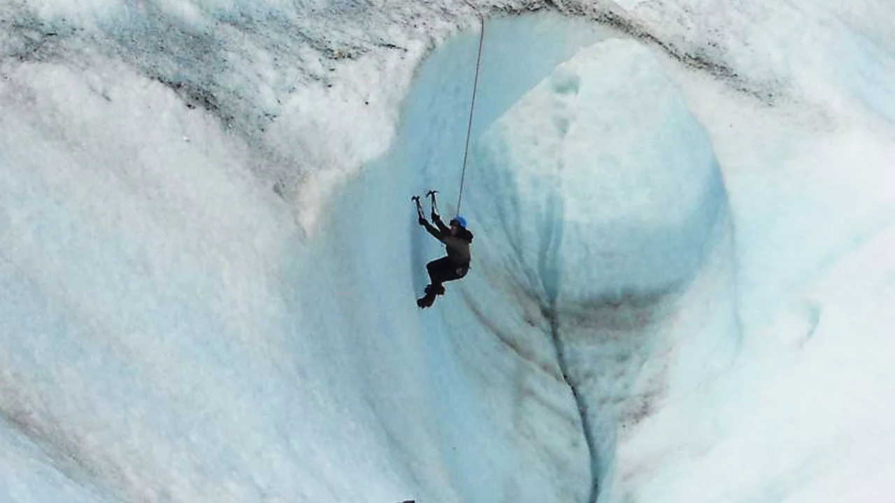 climber climbing on a ice wall with axe and rope attached 