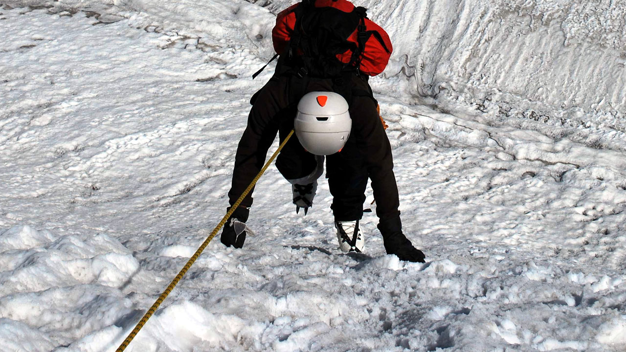 A trainee ice climbing on an ice wall with crampons and a belay line attached