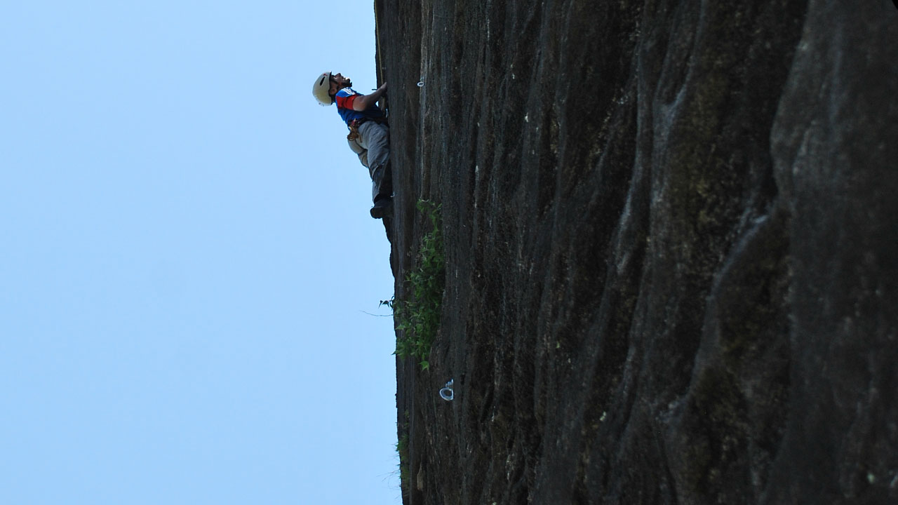 Trainee guiding trad climbing seeking for a hold in the midst of a rock cliff