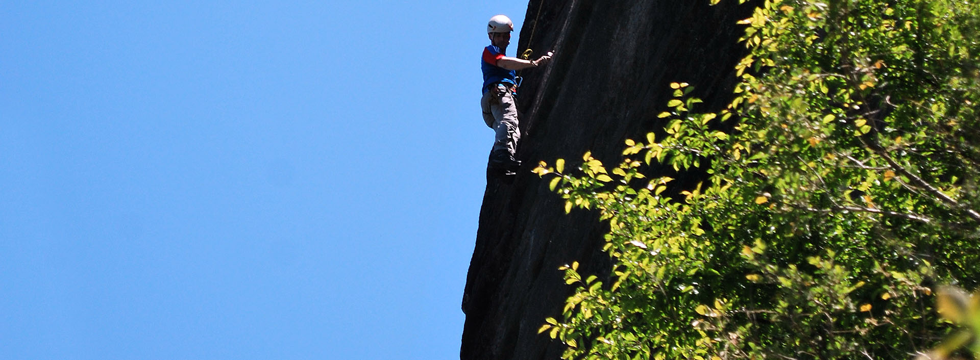 Trainee searching for bolts on high rock in the middle of a lead trad climbing pitch.
