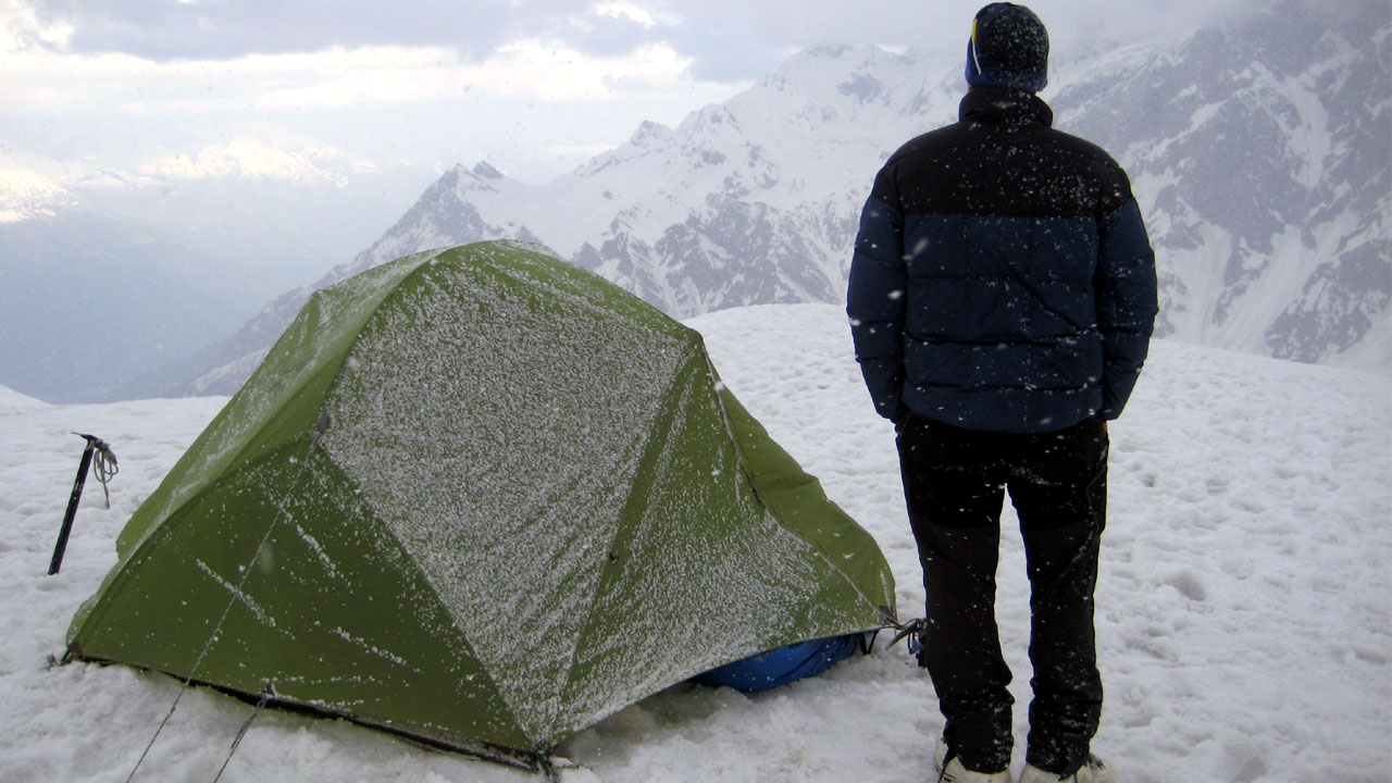 mountain Guide stands outside the tent amid snowfall on Mt Shitidhar in Manali, Himachal Pradesh, looking away from a clearing in the sky