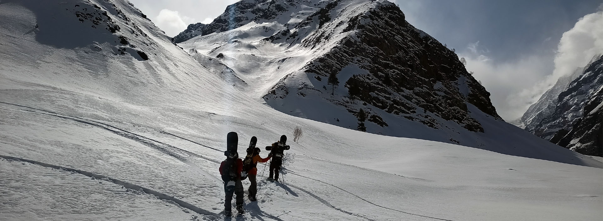 Ski mountaineers with snowboards on their backs walk towards a peak.