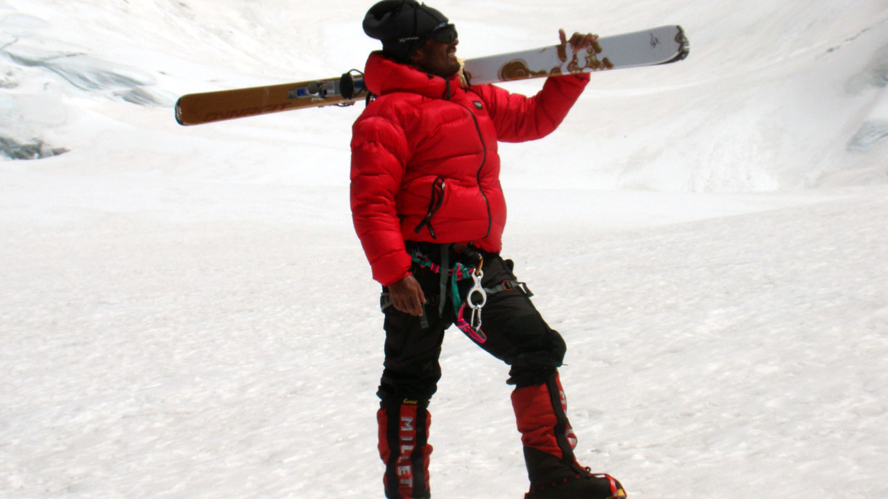 Junna Thakur stands on a steep mountain slope, smiling, with a ski on his shoulders in ski mountaineering