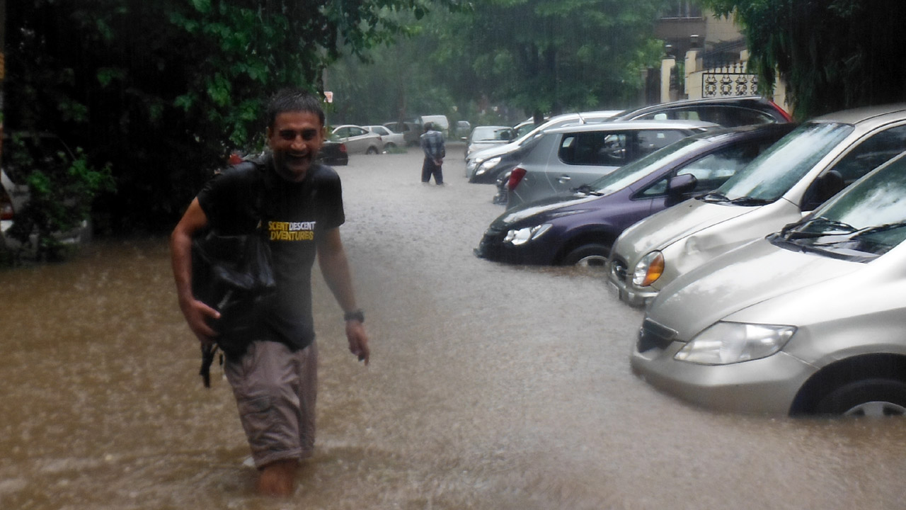 in urban survival situation Pankaj Lagwal smiles in the pouring rain on a flooded road in Delhi, India.