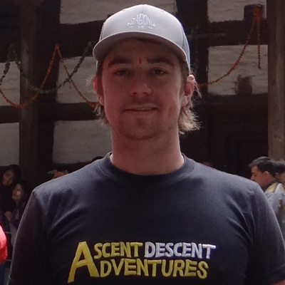 Justin Bower, wearing an Ascent Descent Adventures t-shirt and a hat, stands in front of a Hadimba Temple.