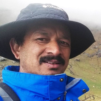 Surender Mahant, dressed in a sun hat and a blue outdoor jacket, smiles with a mustache for his profile photo