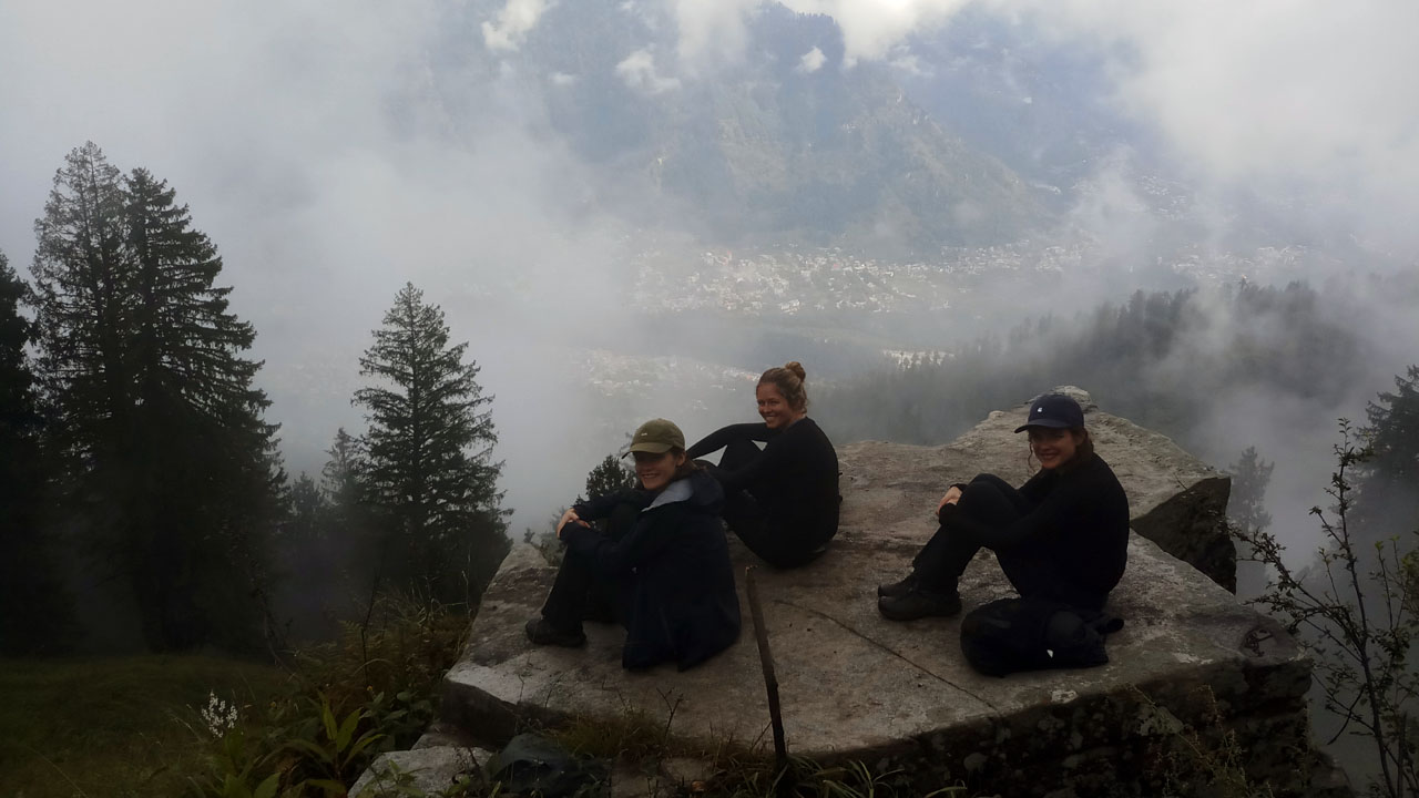 Three female clients pose for a photograph on a rock slab during a day hike in Manali.