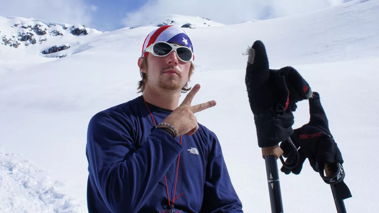 Mountain guide Justin Bower poses for a photo with an American flag bandana on his head and sunglasses, forming the letter V with his fingers