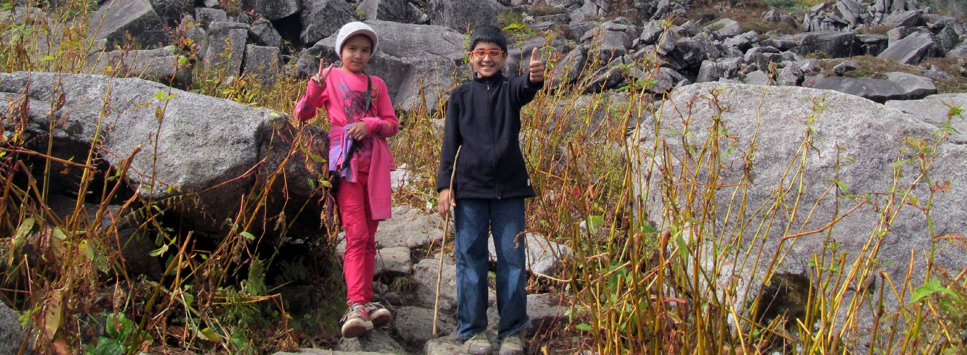 During a day hike in Manali, two children flash thumbs up and a victory sign.