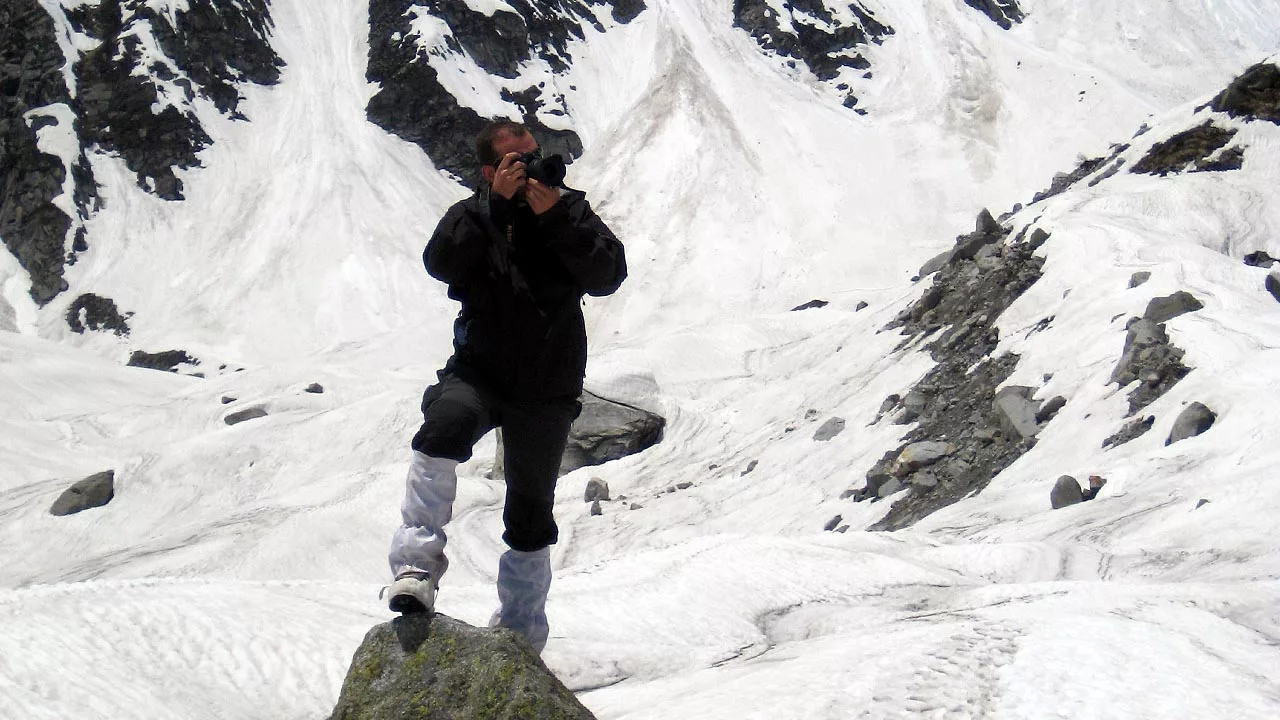 Alpinist Photographing a glacier while standing atop a rock 