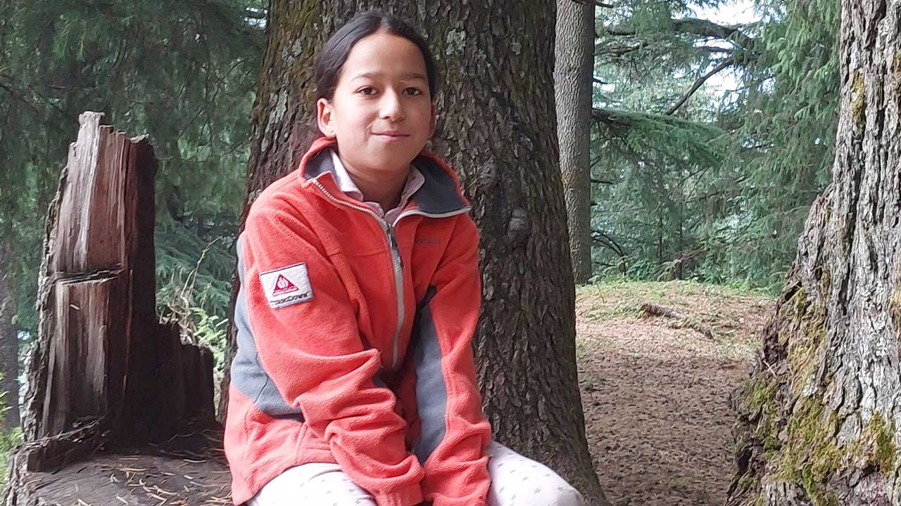 Sadhika sits on a cut tree trunk
