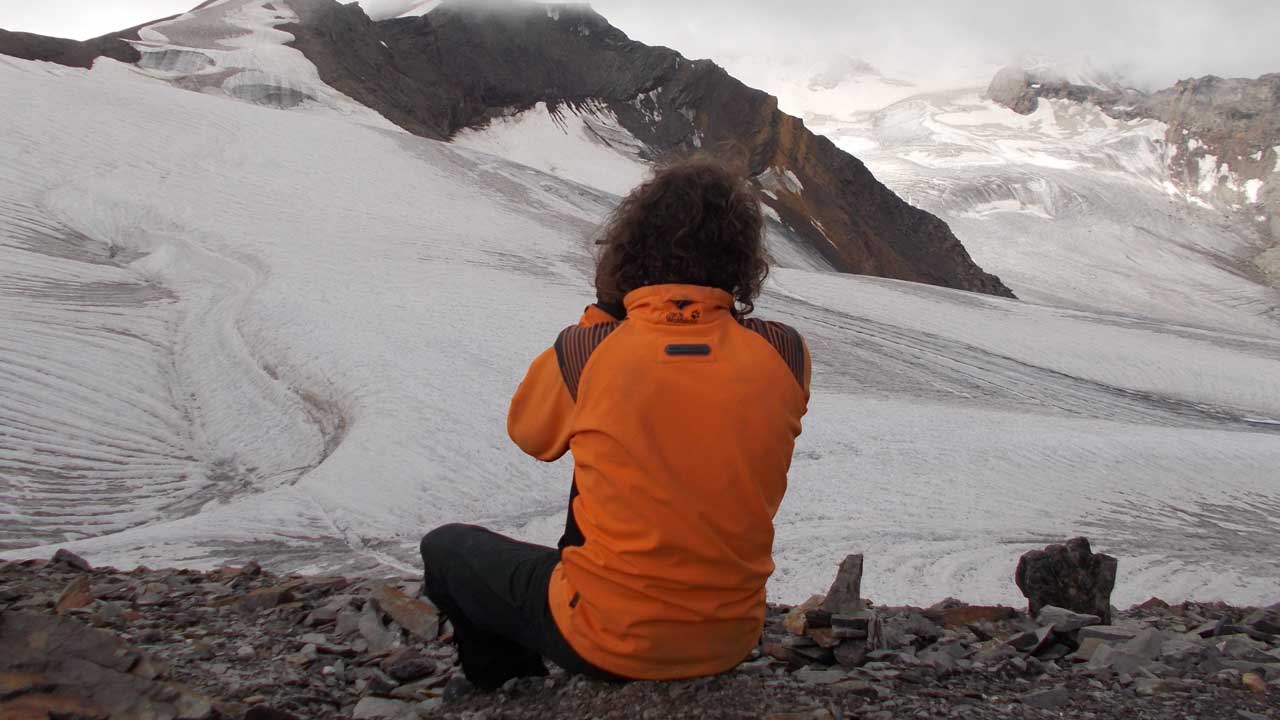 Client sits at Pin Parvati Pass and takes pictures.